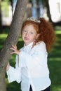 Little girl with red hair in diadem poses near tree Royalty Free Stock Photo