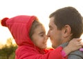 A little girl in a red jacket with a hood hugs and kisses her dad, smiles, touches her nose. Happy family, father`s day, bright ra