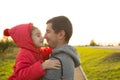A little girl in a red jacket with a hood hugs and kisses her dad, smiles, touches her nose. Happy family, father`s day, bright ra