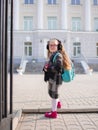 A little girl with red tails before the school, looks into the camera.