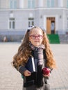 A little girl with red tails on the background of the school.