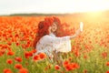 Little girl with redhead mother in white dresses and wreathes make selfie with bouquet of poppies on poppy field at summer sunset