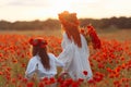 Little girl with redhead mother in white dresses and wreathes walking with bouquet of poppies on poppy field at summer sunset Royalty Free Stock Photo