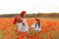 Little girl with redhead mother in white dresses and wreathes walking with bouquet of poppies on poppy field at summer sunset Royalty Free Stock Photo