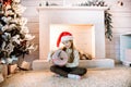 Little girl rejoices gift near the fireplace.Christmas is coming. Home interior christmas tree decoration. santa claus hat