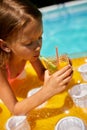 Little girl relaxing in swimming pool, enjoying suntans, drink a juice on inflatable yellow mattress Royalty Free Stock Photo