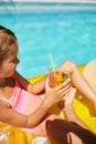 Little girl relaxing in swimming pool, enjoying suntans, drink a juice on inflatable yellow mattress Royalty Free Stock Photo