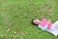 Little girl resting with book lying on green grass with dried leaves in the summer garden Royalty Free Stock Photo