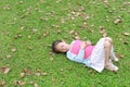 Little girl resting with book lying on green grass with dried leaves in the summer garden Royalty Free Stock Photo