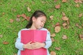 Little girl resting with book lying on green grass with dried leaves in the summer garden Royalty Free Stock Photo