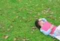 Little girl resting with book lying on green grass with dried leaves in the summer garden Royalty Free Stock Photo