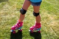 Little girl riding pink four-wheeled roller skates on the grass, knee pads, legs, close-up Royalty Free Stock Photo