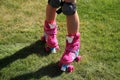 Little girl riding pink four-wheeled roller skates on the grass, knee pads, legs, close-up Royalty Free Stock Photo