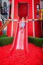 Little girl riding a slide in red plastic balls