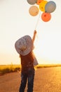 Little girl at road playing with colorful balloons at sunset