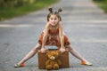 Little girl on the road with a suitcase and a Teddy bear.