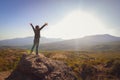 Little girl on a rock in the mountains. The child stretched out his arms towards the sun.