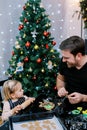 Little girl with a rolling pin sits next to her dad cutting out cookies on the table Royalty Free Stock Photo