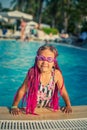A little girl in rose-colored swimming glasses with pink pigtails dressed in a swimsuit jumps out of the pool Royalty Free Stock Photo