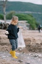 Little girl in rubber boots and gloves with a bag walks through shallow water looking for garbage Royalty Free Stock Photo