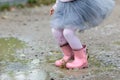 Little girl in rubber boots and tutu dress jumping in puddle. Water is splashing from kid feet as she is jumping and playing in Royalty Free Stock Photo