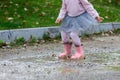 Little girl in rubber boots and tutu dress jumping in puddle. Water is splashing from kid feet as she is jumping and playing in Royalty Free Stock Photo