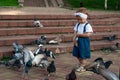 Little girl running near doves, chasing pigeons, happy child with smiling face. Kid is feeding pigeons in city park Royalty Free Stock Photo