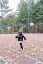 Little girl runs along a basketball court strewn with fallen leaves in the park. Back view