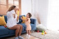 A little girl runs and plays with a small soap bubble that his mother blows for him to play with. In the living room