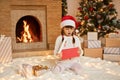 Little girl`s excitement from opening presents on Christmas, female child sitting on floor in santa hat, keeps mouth opened, bein Royalty Free Stock Photo