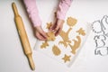 Little girl`s hand making traditional Christmas cookies. Raw dough and cutters for the holiday cookies on a white table. Royalty Free Stock Photo