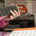 Little girl's hands on the guitar neck handling the fingers on the strings