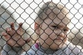 A little girl with a sad look behind a metal fence. The problem of forced deportation of Ukrainian children from the territories