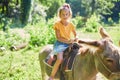 Little girl in the saddle riding on a donkey, in contact farm zoo Royalty Free Stock Photo