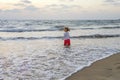 A little girl on a sandy beach against the background of the setting sun went into the sea and looks into the distance,