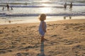 A little girl on a sandy beach looks at the sunset over the sea, the sun`s glare. Royalty Free Stock Photo