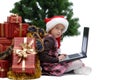 Little girl in Santa Claus cap with a laptop and Christmas gifts Royalty Free Stock Photo