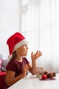 Little girl in Santa hat with Christmas ginger cookies and cup of cacao with marshmallow