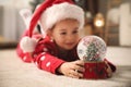 Little girl in Santa hat playing with snow globe on floor Royalty Free Stock Photo