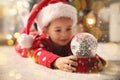 Little girl in Santa hat playing with snow globe on floor. Bokeh effect Royalty Free Stock Photo