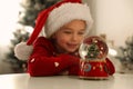 Little girl in Santa hat playing with snow globe at home Royalty Free Stock Photo