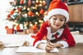 Little girl in Santa\'s hat lying by the New Year tree, writing her heartfelt letter to Santa Claus Royalty Free Stock Photo