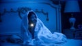 Girl scared of monsters covered in blanket with flashlight