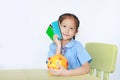 Little girl in school uniform sitting at table showing account book and carry piggy bank isolated over white background. Royalty Free Stock Photo