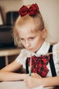 A little girl in a school uniform writes in a notebook with her left hand, does homework at home Royalty Free Stock Photo