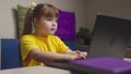 Little girl schooler does homework on laptop at desk in room