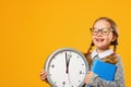 Little girl schoolgirl holds a big clock on a yellow background. The concept of education, development, school, time to learn Royalty Free Stock Photo