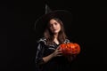 Little girl with a serious expression making a spell while holding a pumpking for halloween