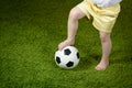 A little girl in shorts put her foot on a soccer ball on a green surface. Royalty Free Stock Photo