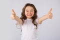 Little girl showing thumbs up gesture in a white T-shirt isolated on white background.